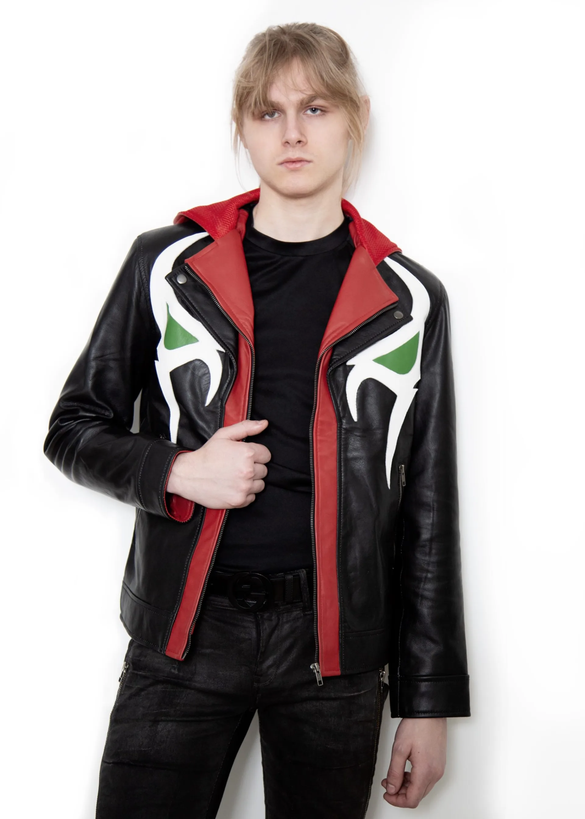 (Front): Photo of a model wearing a black leather jacket. The jacket is a motorcycle cut with a red hood and a red leather lining that is visible inside the cuffs and the folded down collar. There is also a strip of red leather either side of the front zipper. Where breast pockets typically would be on a jacket, there are [handpainted/patched] green eyes surrounded by white details. The collar has metal pop buttons to hold it in place. (Back): Photo of the same black leather jacket with a red hood. The jacket is a motorcycle cut. The inside of the hood has a mesh lining.